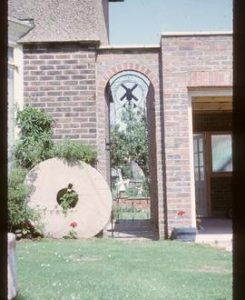 Millstone in garden, beside gate with windmill design