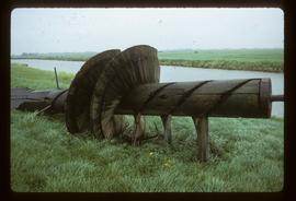 Wooden Archimedean screw-like device lying by side of dyke/polder